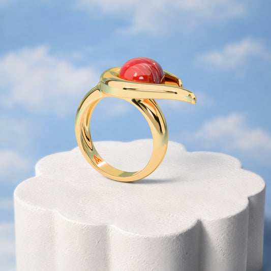 Anel Órbita - Feldspato Vermelho: sobre pedestal de gesso em forma de nuvem, fundo de céu azul-claro. Semijoia banhada a ouro 18k, coleção Supernova, Aimer Joias