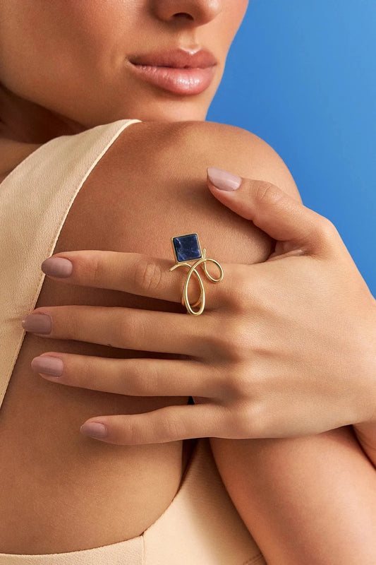 O Anel Esboço com Sodalita em Banho de Ouro 18K traduz a união entre linhas e formas, em um desenho limpo e simbólico. A pedra quadrada de Sodalita, que se equilibra de forma leve no traço orgânico da peça, simboliza clareza e intuição. O equilíbrio entre a forma geométrica da pedra e o traço orgânico do aro confere à peça um charme contemporâneo, perfeito para destacar sua mão com sofisticação.