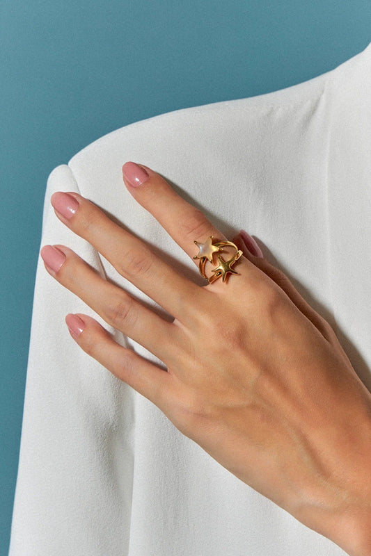 O Anel Estelar com Ágata Branca em Banho de Ouro 18K possui duas estrelas-do-mar que se encontram na mesma direção, simbolizando harmonia e união. A pureza da Ágata Branca é realçada pelo luxo do ouro, criando um visual sofisticado e marcante.