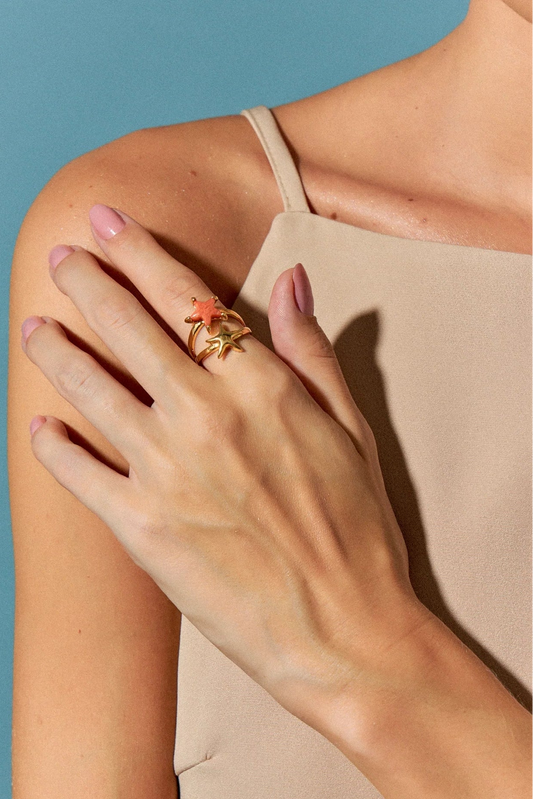 O Anel Estelar com Feldspato Laranja em Banho de Ouro 18K possui duas estrelas-do-mar que se encontram na mesma direção, simbolizando harmonia e união. A tonalidade vibrante do Feldspato Laranja é realçada pelo luxo do ouro, criando um visual sofisticado e cheio de energia.