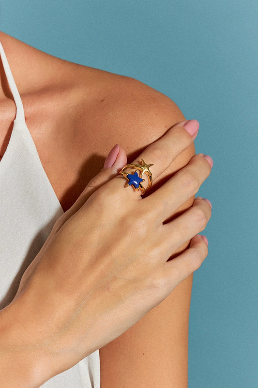 O Anel Estelar com Quartzo Azul Anil em Banho de Ouro 18K possui duas estrelas-do-mar que se encontram na mesma direção, simbolizando harmonia e união. O tom profundo do Quartzo Azul Anil, em contraste com o brilho do ouro, cria um visual sofisticado que evoca a cor do oceano.