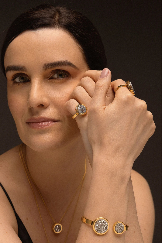 O Anel Eterno - Drusa Platina, da Coleção Singular, é uma joia que une a força da natureza bruta ao luxo do acabamento polido. A Drusa Platina é reconhecida por sua capacidade de amplificar energias positivas, promover o equilíbrio e trazer brilho pessoal. Banhado a Ouro 18K, este anel de design contínuo destaca a textura cristalizada e o brilho metálico da pedra, criando uma peça imponente e luminosa, perfeita para mulheres que buscam um acessório de personalidade marcante.