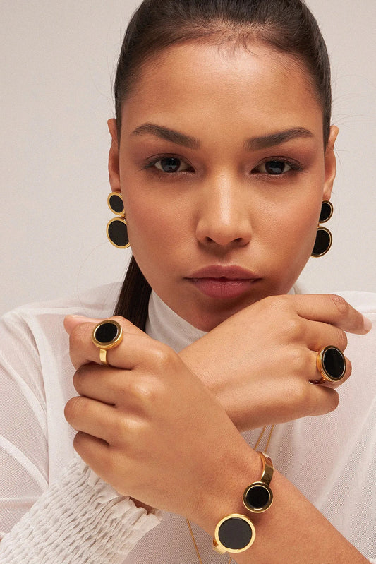 O Anel Eterno - Obsidiana Negra, integrante da Coleção Singular, é uma joia de magnetismo profundo e elegância absoluta. A Obsidiana Negra é uma poderosa pedra de proteção, aterramento e escudo contra energias negativas, favorecendo a força interior. Banhado a Ouro 18K, este anel de design contínuo cria um contraste luxuoso entre o negro intenso da pedra e o brilho do ouro, resultando em uma peça imponente e atemporal para mulheres de presença marcante.