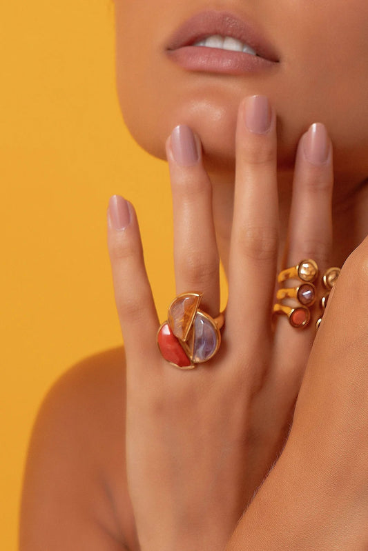 O Anel Impacto em Banho Ouro 18K une a energia de três cristais poderosos: o Citrino, para prosperidade e sucesso; a Ametista, para sabedoria e proteção espiritual; e o Feldspato Laranja, que atrai vitalidade e criatividade. Esta peça de design imponente combina o sucesso no amor, a prosperidade e a sabedoria em uma única joia.