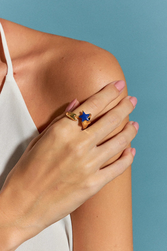 O Anel Serena com Quartzo Azul Anil em Banho de Ouro 18K possui duas estrelas-do-mar que se encontram na mesma direção, simbolizando harmonia e união. O tom profundo do Quartzo Azul Anil, em contraste com o brilho do ouro, cria um visual delicado, mas marcante, que evoca a serenidade do oceano.