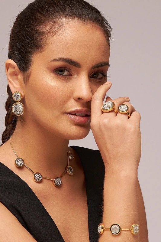 O Anel Único - Drusa Platina integra a Coleção Singular, celebrando a nobreza e a força da mulher. A Drusa Platina é uma pedra fascinante que auxilia na amplificação de energias, no equilíbrio emocional e no fortalecimento do brilho pessoal. Banhado a Ouro 18K, este anel une a sofisticação do banho dourado com a textura orgânica da drusa, resultando em uma joia imponente e cheia de significado.