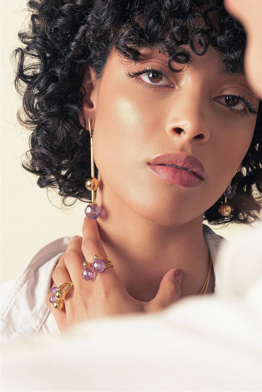 O Brinco Fascínio em Ametista, com Banho de Ouro 18K, possui um visual clássico e luxuoso. A Ametista, com seu tom roxo intenso, oferece um acabamento delicado e marcante, realçado pelo brilho do ouro.