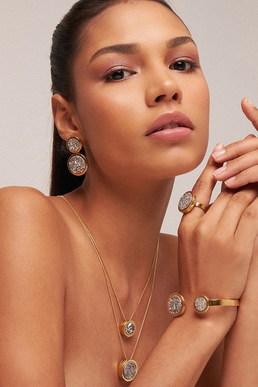 O Brinco Nobre - Drusa Platina, integrante da Coleção Singular, é uma joia de impacto visual extraordinário que une o estado bruto da natureza ao luxo do ouro. A Drusa Platina é valorizada por sua capacidade de amplificar energias positivas, promover o equilíbrio e destacar o brilho pessoal de quem a usa. Banhado a Ouro 18K, este brinco de design imponente ressalta a textura cristalizada e o reflexo metálico único da pedra, resultando em uma peça sofisticada e cheia de personalidade para ocasiões marcantes.