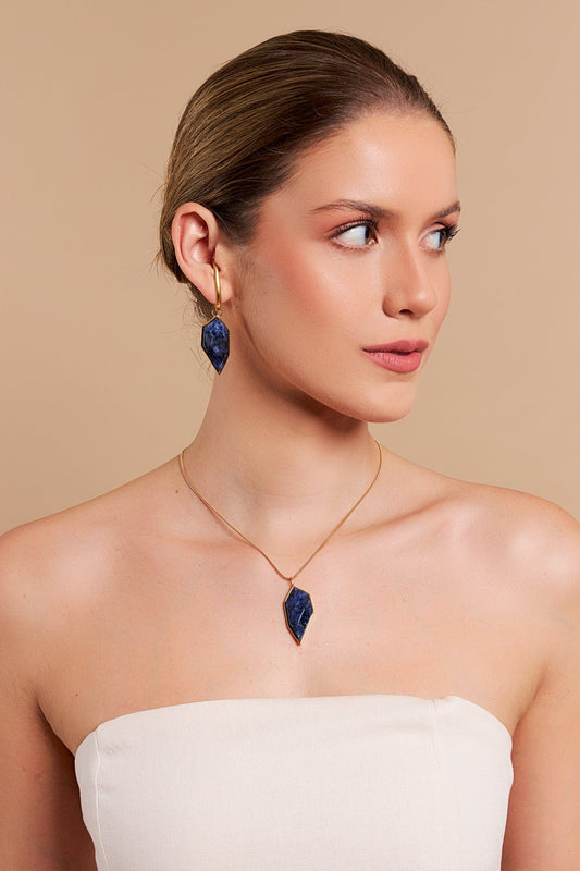 Colar Impulso - Modelo usando um conjunto de joias com pedras de Sodalita Azul em formato geométrico, incluindo colar e brincos, todos banhados em ouro 18k