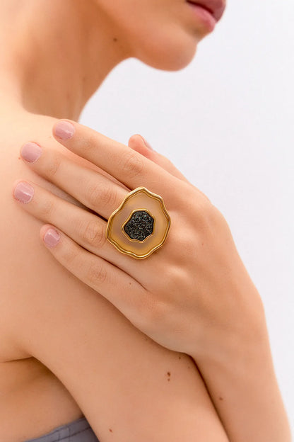 Esta joia combina o contraste de cores clássico com forte simbologia, sendo adornada com Ágata Branca, que promove a paz e a clareza, e Drusa Negra, que atrai energia positiva e proteção. Use este anel em Banho de Ouro 18K para celebrar o seu próprio florescer com elegância.