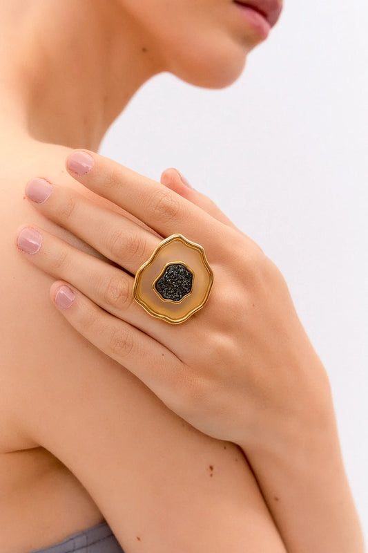 Esta joia combina o contraste de cores clássico com forte simbologia, sendo adornada com Ágata Branca, que promove a paz e a clareza, e Drusa Negra, que atrai energia positiva e proteção. Use este anel em Banho de Ouro 18K para celebrar o seu próprio florescer com elegância.