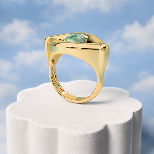 Anel Despertar - Quartzo Verde: sobre pedestal de gesso em forma de nuvem, fundo de céu azul-claro. Semijoia banhada a ouro 18k, coleção Supernova, Aimer Joias