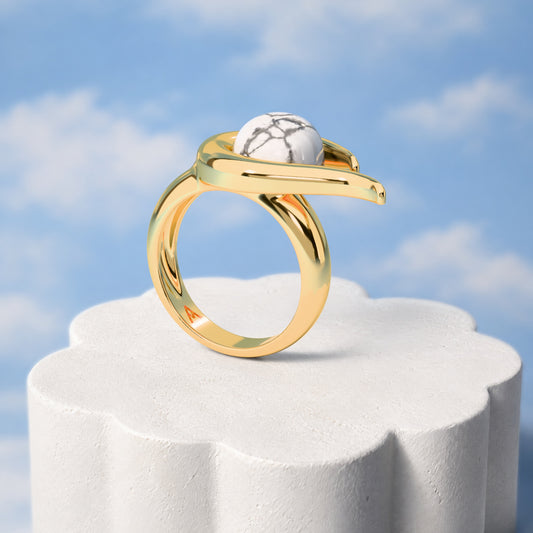 Anel Órbita - Howlita Branca: sobre pedestal de gesso em forma de nuvem, fundo de céu azul-claro. Semijoia banhada a ouro 18k, coleção Supernova, Aimer Joias