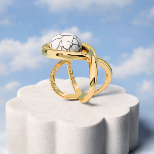 Anel Supernova - Howlita Branca: sobre pedestal de gesso em forma de nuvem, fundo de céu azul-claro. Semijoia banhada a ouro 18k, coleção Supernova, Aimer Joias