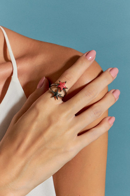 O Anel Estelar com Feldspato Vermelho em Banho de Ródio Negro possui duas estrelas-do-mar que se encontram na mesma direção, simbolizando harmonia e união. A cor intensa do Feldspato Vermelho, em contraste com o brilho escuro e metálico do Ródio Negro, cria um visual sofisticado e marcante.