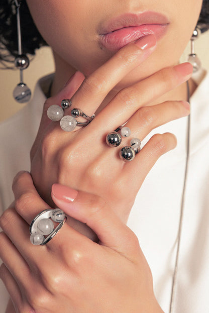 O Anel Sublime em Esmaltado Branco e Quartzo Grafitado, com Banho de Ouro 18K, é uma peça de contraste clássico e sofisticado. O Quartzo Grafitado Liso harmoniza-se com o esmalte branco, criando um visual elegante e atemporal com o brilho do ouro.