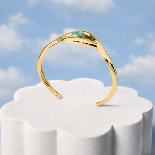 Bracelete Despertar - Quartzo Verde: sobre pedestal de gesso em forma de nuvem, fundo de céu azul-claro. Semijoia banhada a ouro 18k, coleção Supernova, Aimer Joias
