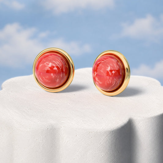 Brinco Aurora - Feldspato Vermelho: sobre pedestal de gesso em forma de nuvem, fundo de céu azul-claro. Semijoia banhada a ouro 18k, coleção Supernova, Aimer Joias