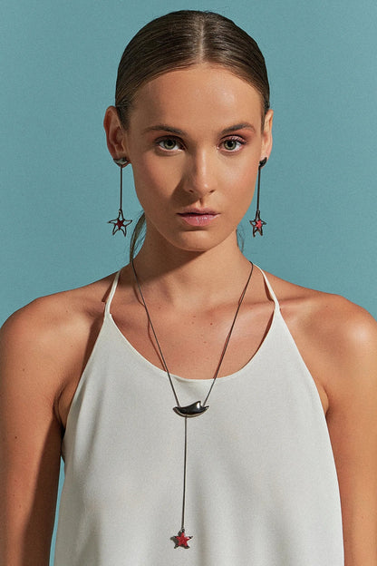 Use o Brinco Brisa com Feldspato Vermelho em Banho de Ródio Negro, criando um contraste dramático e luxuoso entre o tom vibrante da pedra e o acabamento escuro e moderno do ródio.