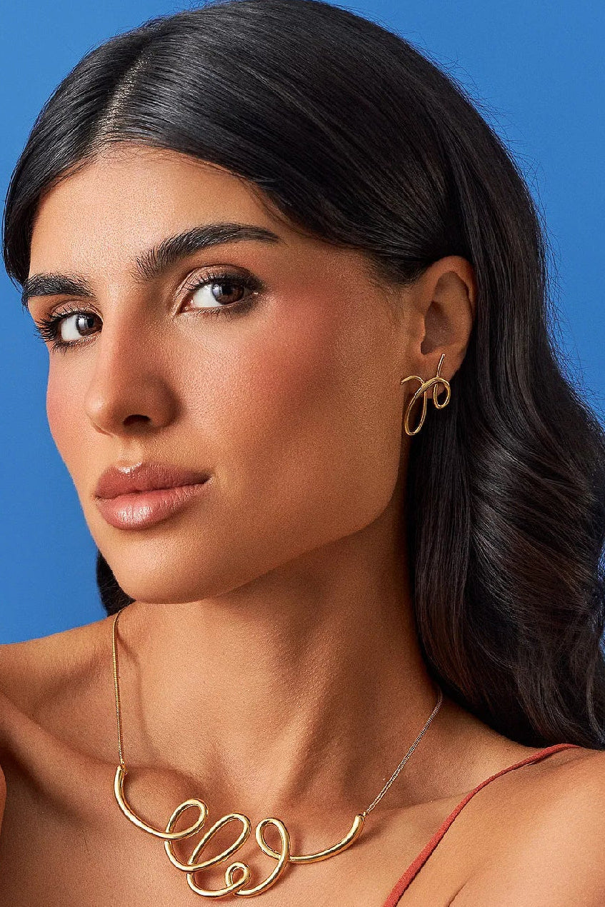 O Brinco Rabiscos em Banho de Ouro 18K traduz a magia do risco que se arrisca a ser algo, com formas orgânicas e minimalistas. Este brinco celebra a beleza do gesto livre e expressivo, sendo uma peça discreta, mas que carrega movimento e significado. É a essência da Coleção Entre o Traço e a Forma.