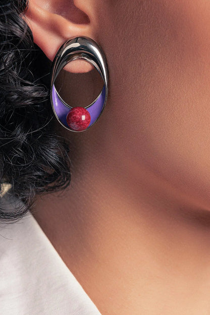 O Brinco Sinergia em Esmaltado Roxo e Feldspato Vermelho, com Banho de Ródio Negro, cria um visual de impacto. A combinação vibrante do vermelho com o roxo é realçada pelo luxuoso acabamento escuro do ródio negro.