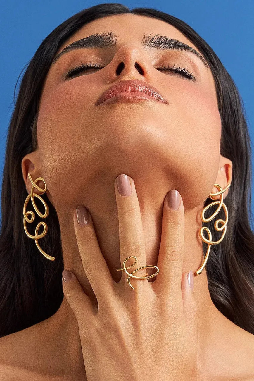 O Brinco Traços em Banho de Ouro 18K é uma joia escultural e assimétrica, inspirada em linhas livres que se encontram, criando volumes fluidos. Um lembrete de que o belo não nasce do controle absoluto, mas do gesto que ousa sair do traço e encontra uma nova forma de ser. São peças leves, expressivas e cheias de movimento.